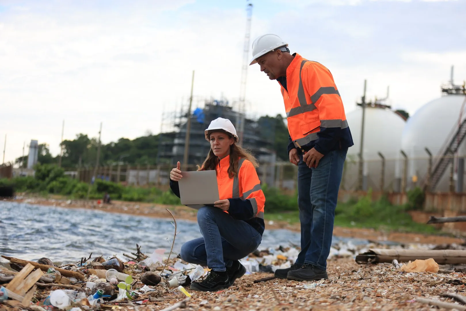 A chief petrochemical engineer and a senior engineer in safety coveralls reviewing oil and gas production performance on a laptop